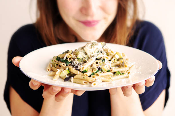 młoda kobieta trzymająca biały talerz z makaronem i serem - pesto sauce italian culture pine nut photography zdjęcia i obrazy z banku zdjęć