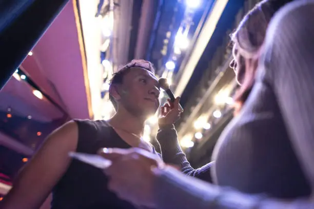 Male ballet dancer getting a retouch on his make up from a professional make up artist backstage