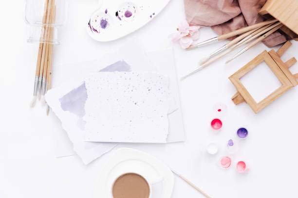 istock Flat lay art workspace, sheet of paper with paints and brushes on white table 957028370