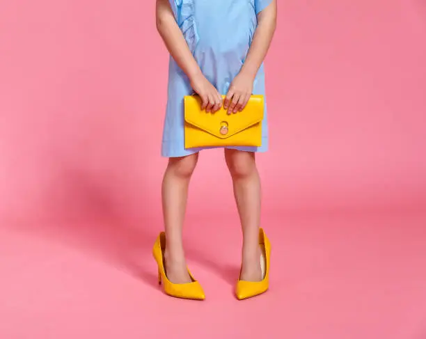 Photo of child girl's legs in large high heeled shoes on colored background