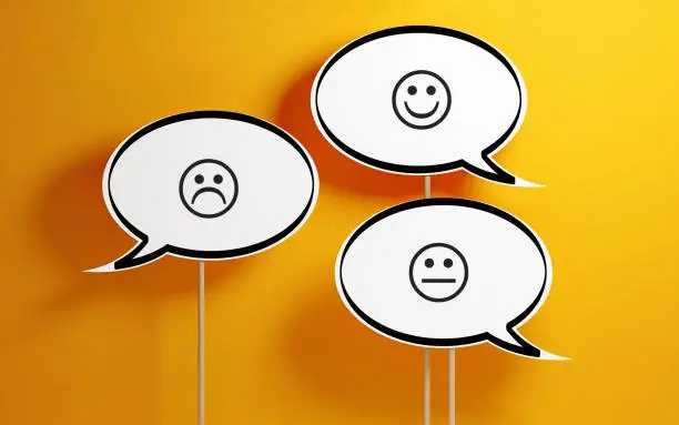 White chat bubble with wooden stick on yellow background. There are various smiley faces on the speech bubbles. Horizontal composition with copy space.