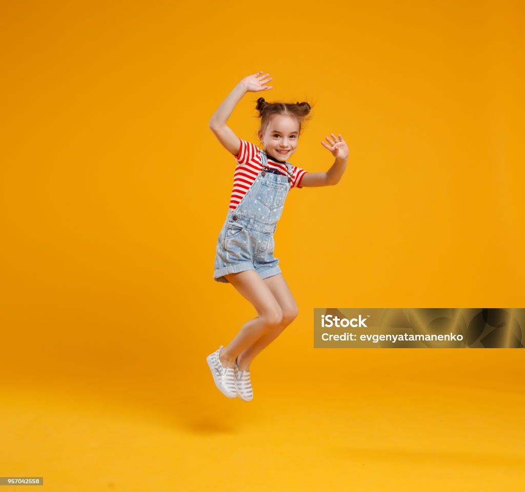 fille de drôle enfant sautant sur fond jaune coloré - Photo de Enfant libre de droits