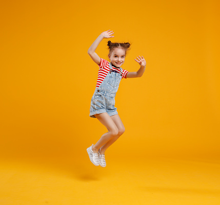 funny child girl jumping on a colored yellow background
