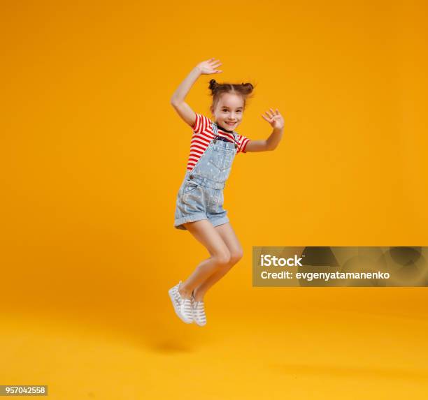 Funny Child Girl Jumping On Colored Yellow Background Stock Photo - Download Image Now