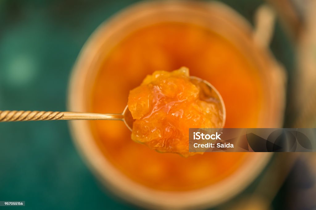 Orange jam in a tea spoon Upper view shot of a tea spoon with orange jam held above a blurred jar with orange jam. Shot with shallow depth of field. Quince Stock Photo