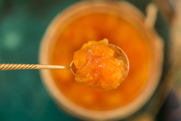 Orange jam in a tea spoon Upper view shot of a tea spoon with orange jam held above a blurred jar with orange jam. Shot with shallow depth of field. marmalade stock pictures, royalty-free photos & images