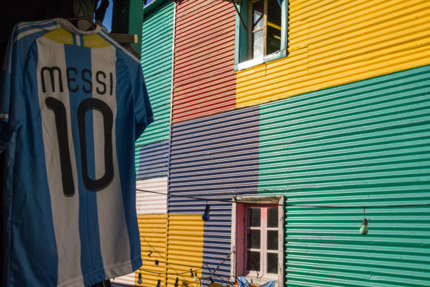 аргентинская рубашка лионеля месси выставлены рядом с красочными зданиями окрестности ла бока в буэнос-айресе, - messi argentina стоковые фото и изображения