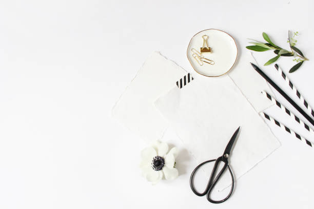 istock Breakfast or birthday party desktop scene. Composition with empty milk glass jar, black and white drinking paper straws and anemone flower.White table background. Flat lay, top view. 957080104