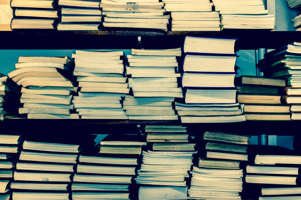 The battered ends of old, neglected books stacked on wooden shelving.  Belfast, Northern Ireland.  Cross-processed.