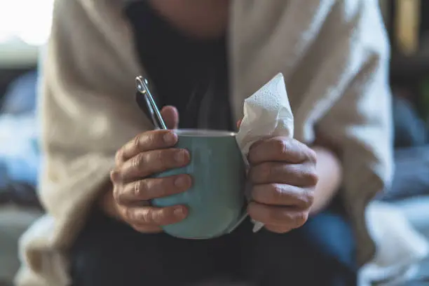 A young man that has caught a cold is at home holding a mug of hot tea.