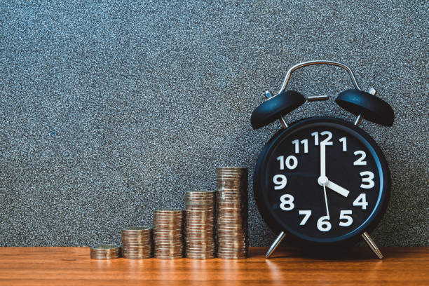 istock Alarm clock and step of coins stacks on working table, time for savings money concept. 957100098