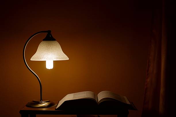 Closeup of a black desk lamp illuminating an open lined notepad and ballpoint pen on a black background