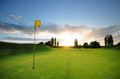 Golfer putting ball on the green golf, lens flare on sun set evening time. Golfer action to win after long putting golf ball in to the hole.