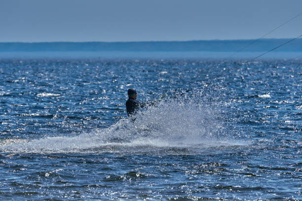 istock A male kiteboarder rides on a board on a large river. He performs various exercises while moving on water. Splashes of water scatter in different directions. The sun's rays shine in the water. Sunny spring day. 957115586