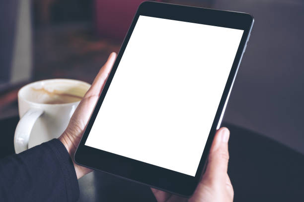 istock Top view mockup image of hands holding black tablet pc with white blank screen and coffee cup on table background 957116464