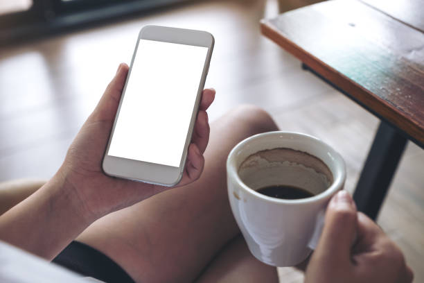 istock Mockup image of woman holding white mobile phone with blank screen while drinking coffee in cafe 957116792