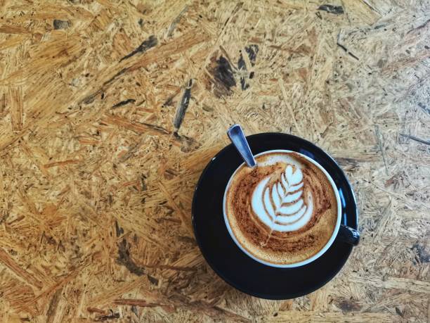Hot latte coffee art in black cup on a plywood table