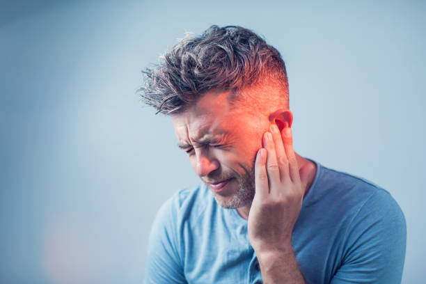 male having ear pain touching his painful head isolated on gray background - tinitus imagens e fotografias de stock