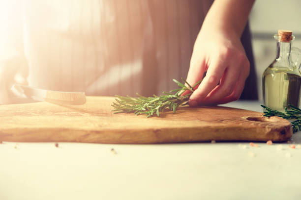 Woman hands cutting fresh green rosemary on wood chopping board in white kitchen, interior. Copy space. Homemade food conceplt, healthy recipe. Take me to work
