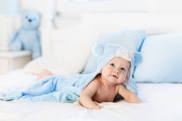 istock Baby boy in blue towel on white bed 957143936
