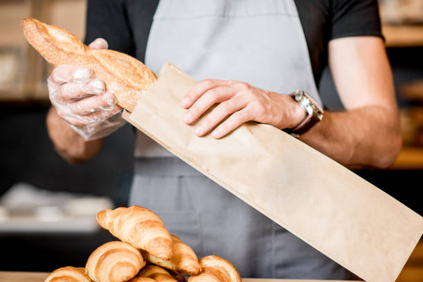 Packing bread into the paper bag Seller packing bread into the paper bag in the bakery shop, close-up view on the bag with copy space bread bakery baguette french culture stock pictures, royalty-free photos & images