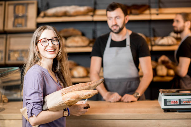 Woman buying bread in the bakery shop with man sellers Portrait of a happy woman client buying bread at the bakery shop with handsome male sellers bread bakery baguette french culture stock pictures, royalty-free photos & images