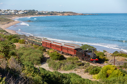 Victor Harbor, Australia, April 19, 2018:  SteamRanger Heritage Railway's steam-hauled Cockle Train with Rx207 passing along southern coastline near Victor Harbor with Port Elliot in the background