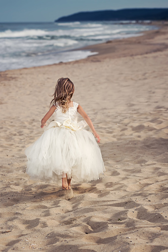 Beautiful little girl in a white dress on the background of the sandy beach of the Black Sea