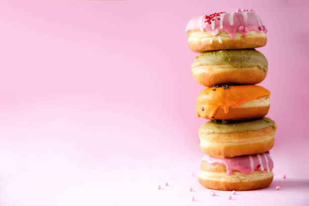 istock Stack of glazed colorful assorted donuts with sprinkles on pink background. Copy space. Sweet doughnuts for kids 957167682