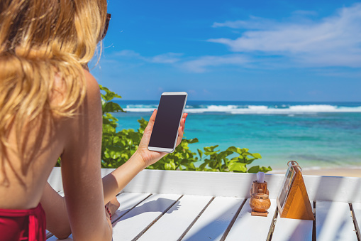 Girl using cellphone in the restaurant on a exotic tropical beach.