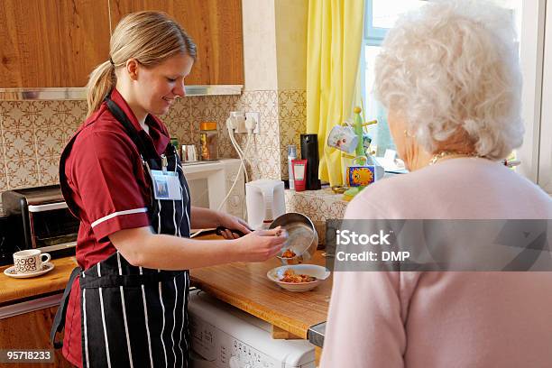 Młoda Pielęgniarka Gotowanie Dla Starszy Kobieta W Jej Kuchni - zdjęcia stockowe i więcej obrazów Gotować