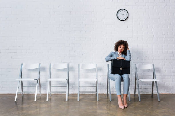 znudzona kobieta z teczką siedząca na krześle i czekająca - waiting women clock boredom zdjęcia i obrazy z banku zdjęć