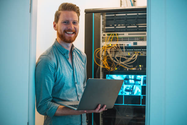 Male Caucasian IT technician using laptop in server room stock photo