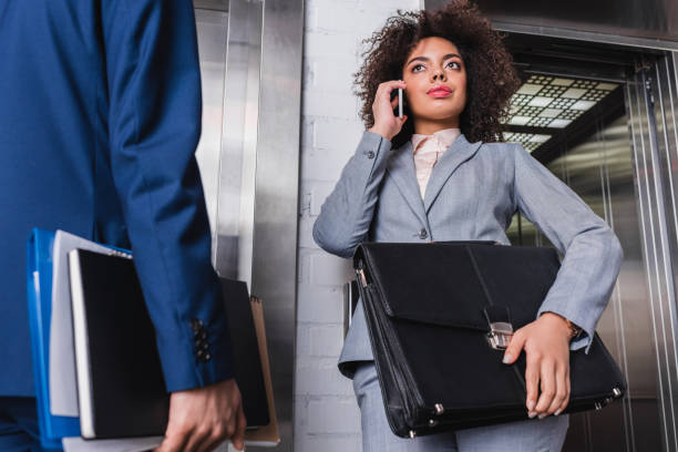 istock Businesswoman with briefcase talking on the phone next to man by elevator 957204638