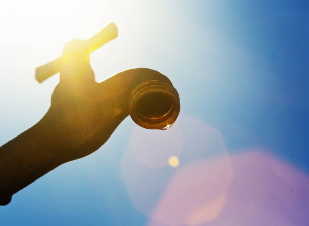 Low-angle look at a dripping tap against blazing hot sun, symbolizing drought and water wastage.