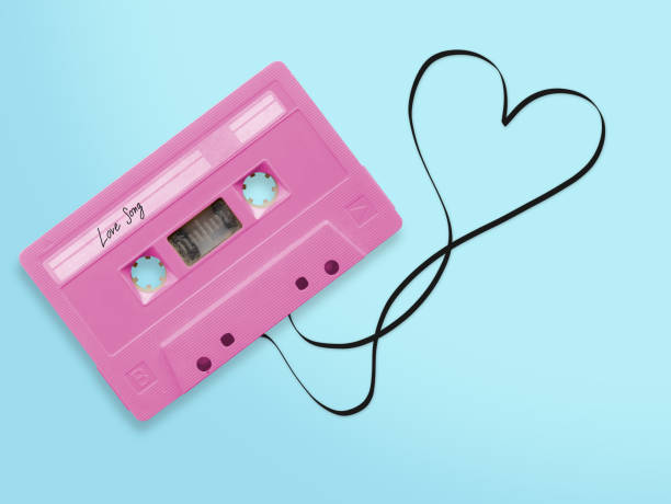 pink audio cassette tape with label tag love song tangled tape ribbon heart shape isolated on blue background, top view. pink audio cassette tape with label tag love song tangled tape ribbon heart shape isolated on blue background, top view. mix tape heart stock pictures, royalty-free photos & images