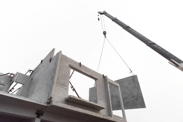 istock Construction site crane is lifting a precast concrete wall panel to installation building. 957223332