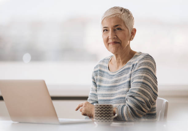 istock Smiling mature woman using computer during coffee time at home. 957232942