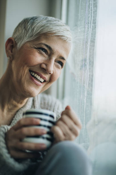 istock Happy senior woman with tea cup looking through window. 957233858