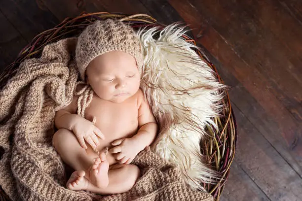 Photo of Beautiful little newborn boy 20 days  sleeps in a basket whith knitted plaid. Portrait of pretty newborn boy