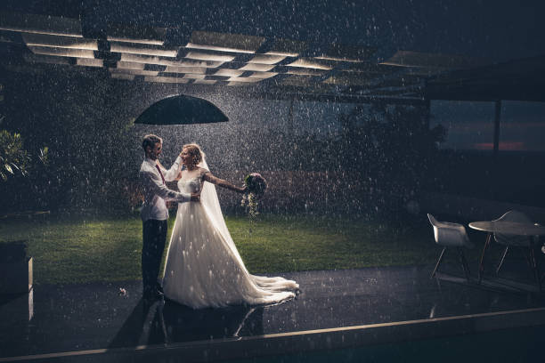 longitud total de recién casados felizes bajo el paraguas durante la lluvia. - face to face twilight togetherness vertical fotografías e imágenes de stock