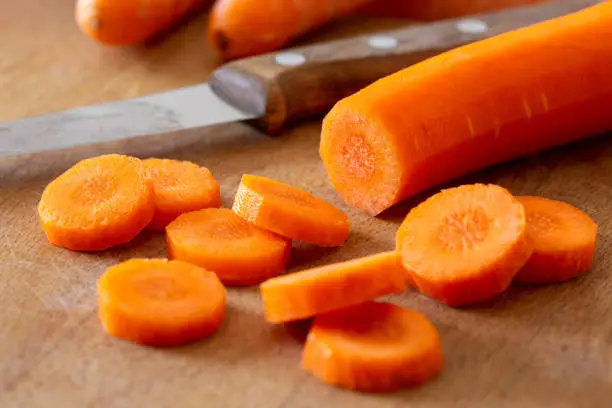 Sliced peeled carrot next to a knife on wood chopping board.