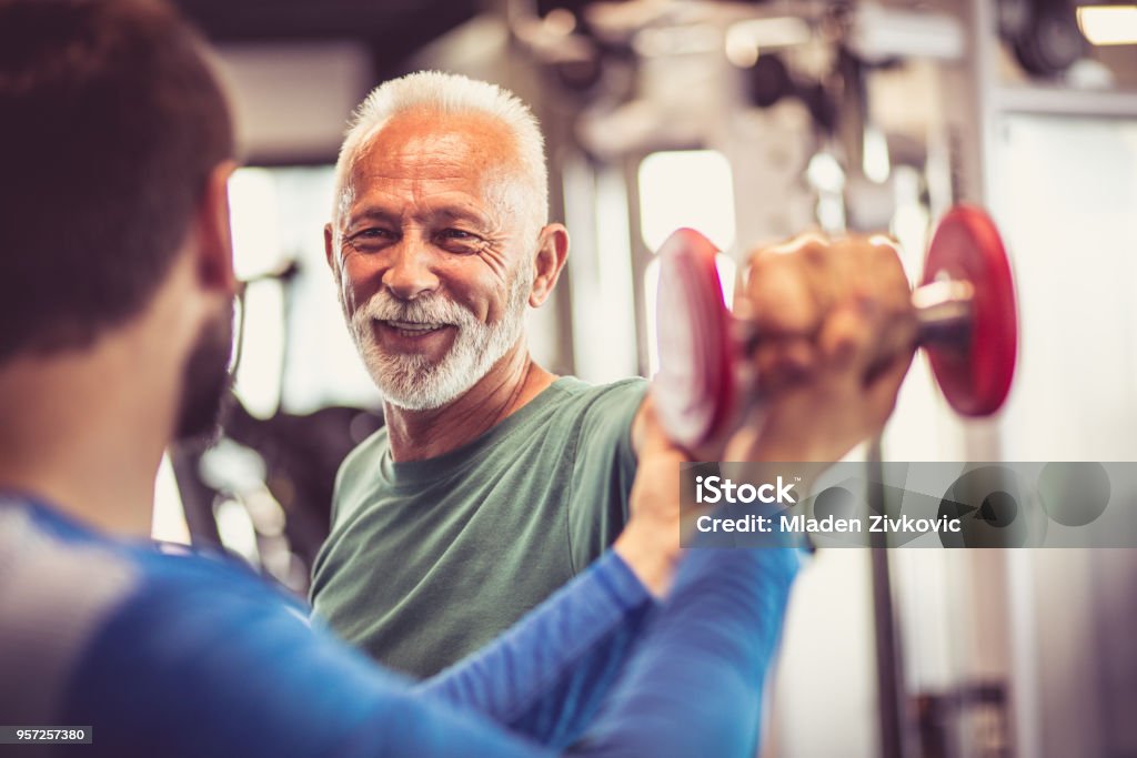 Weight in hand. Fitness instructor helping senior man  in exercise. Focus is on hand. Close up. Fitness Instructor Stock Photo