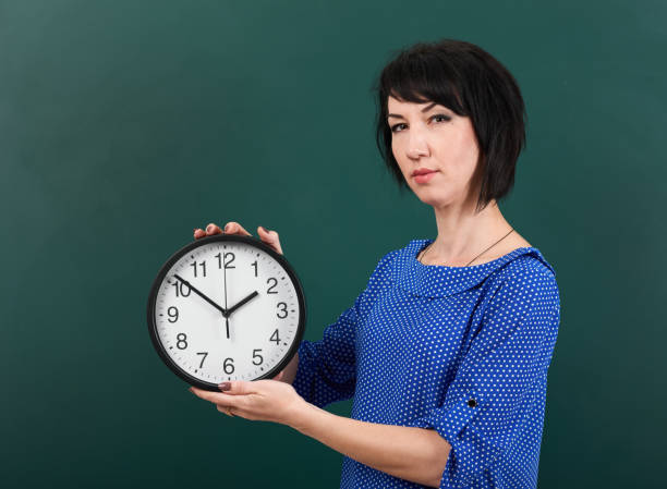 istock woman student with big clock posing by chalk Board, education concept, green background, studio shot 957262876