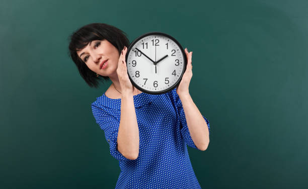 istock woman with big clock posing by chalk board, time and education concept, green background, studio shot 957265514