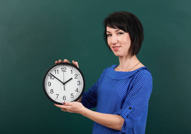 istock woman student with big clock posing by chalk Board, education concept, green background, studio shot 957265900