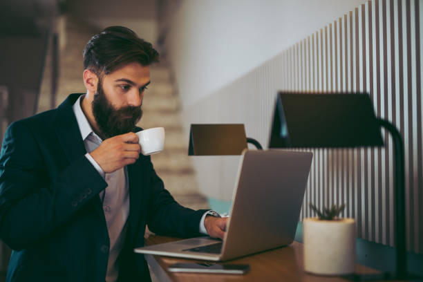 istock Relaxed young businessman having coffee while working on laptop 957275762