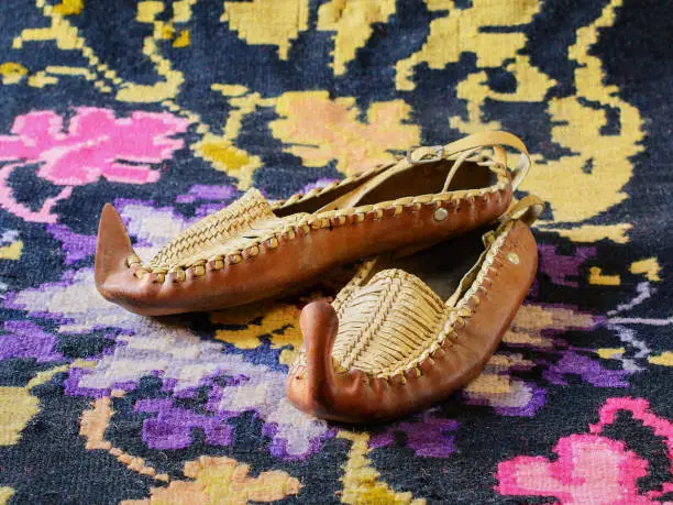 Opanci, traditional handcrafted leather folk shoes, a part of the Serbian national costume, are lying on a kilim, a traditional handmade flat-woven floor rug. Selective focus.
