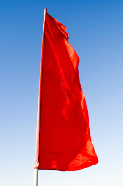 istock Red flag of rectangular shape elongated fluttering in the wind on the flagpole background of the blue sky. 957292674