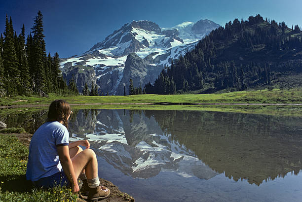 Young Female Hiker at Aurora Lake with Mt Rainier Reflection This young female hiker is enjoying the view of Mount Rainier reflected in Aurora Lake. This photograph was taken at Klapatche Park in Mount Rainier National Park, Washington State, USA. jeff goulden mount rainier national park stock pictures, royalty-free photos & images